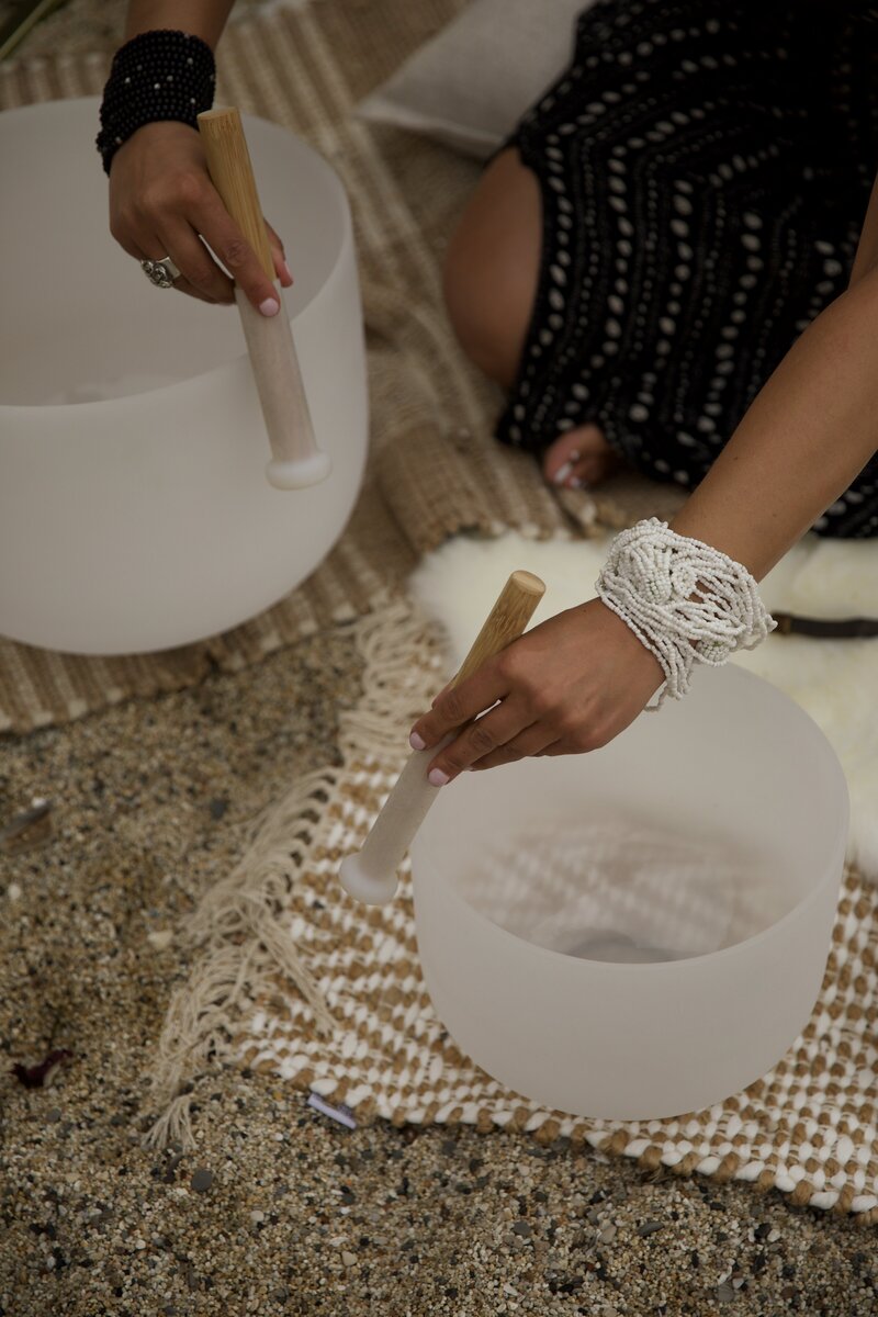 Hands playing crystal singing bowls on a woven mat