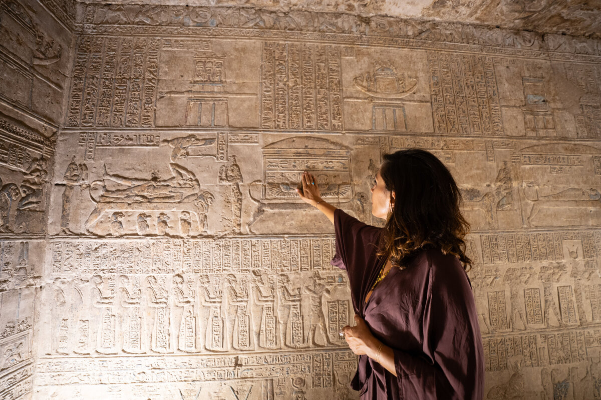 A woman standing before carved reliefs inside an Egyptian temple