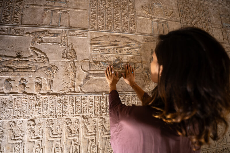 Woman touching carved reliefs inside an Egyptian temple