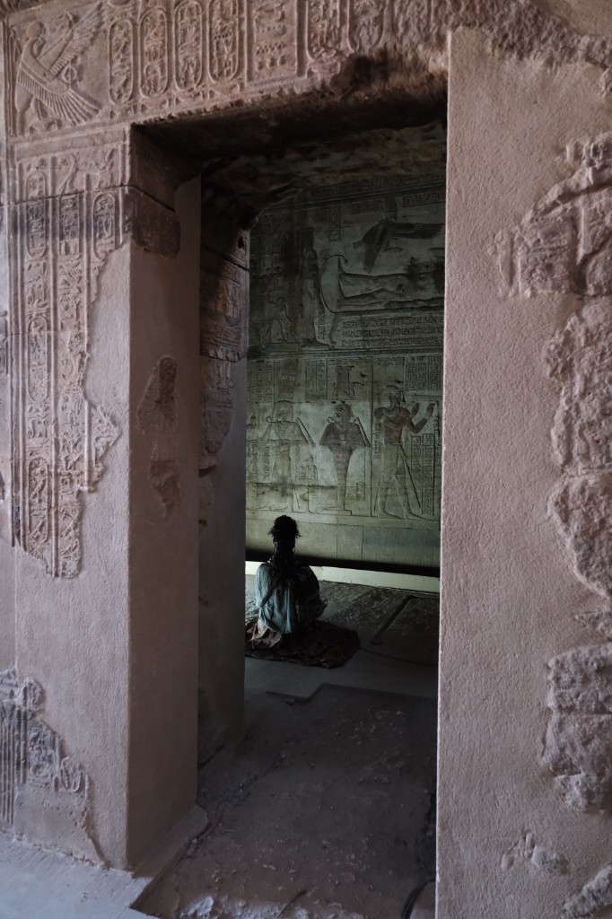 A pilgrim seated in meditation inside an ancient Egyptian temple chamber, framed by a carved stone doorway