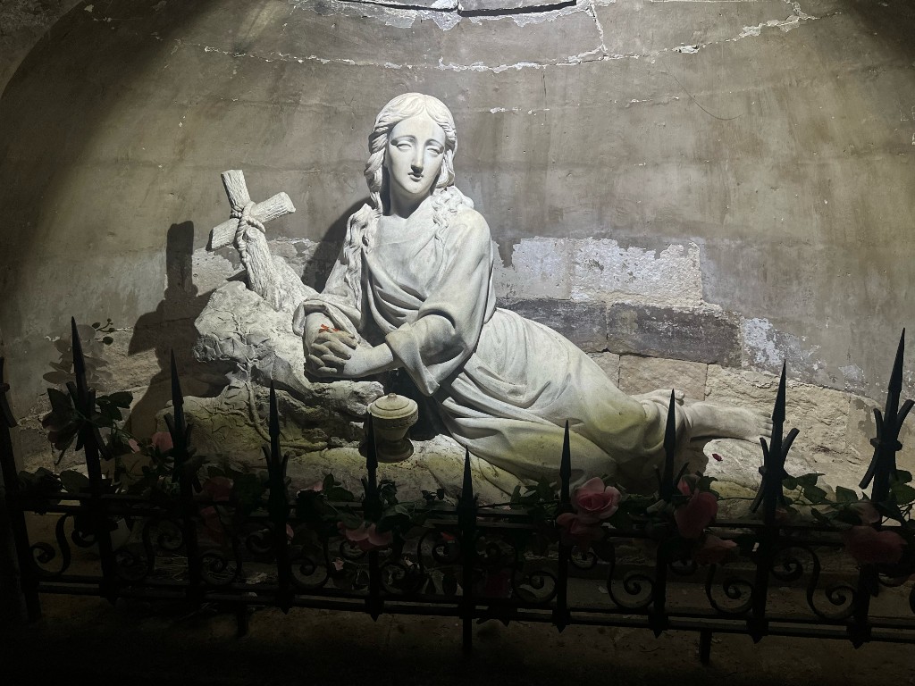 Mary Magdalene statue in a stone grotto behind an iron gate with roses
