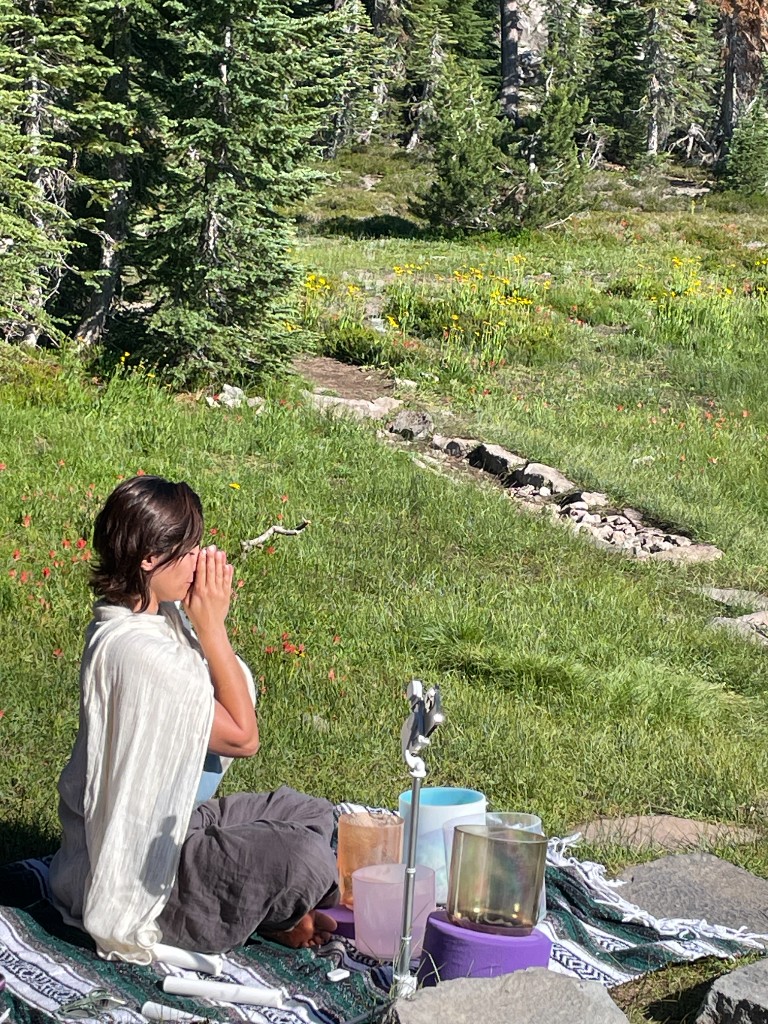 Tolo in prayer on a meadow at Mount Shasta with crystal singing bowls among the pines